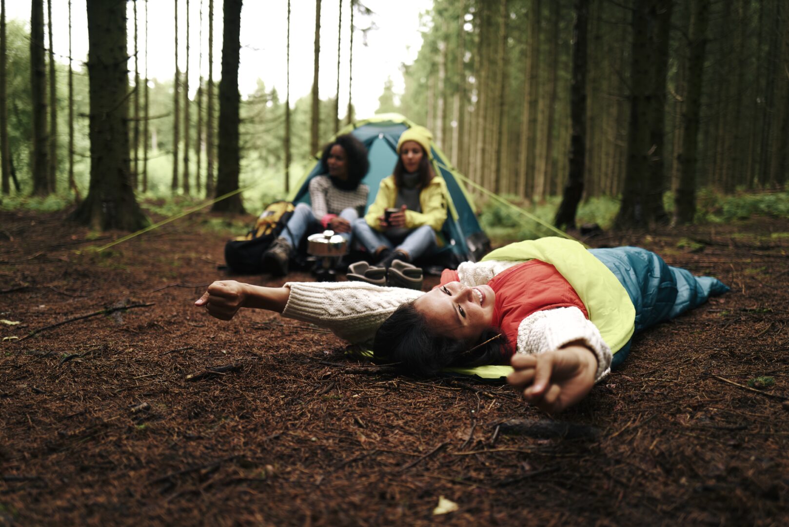 3 Menschen, die in einem Wald mit Schlafsack und Zelt übernachten.