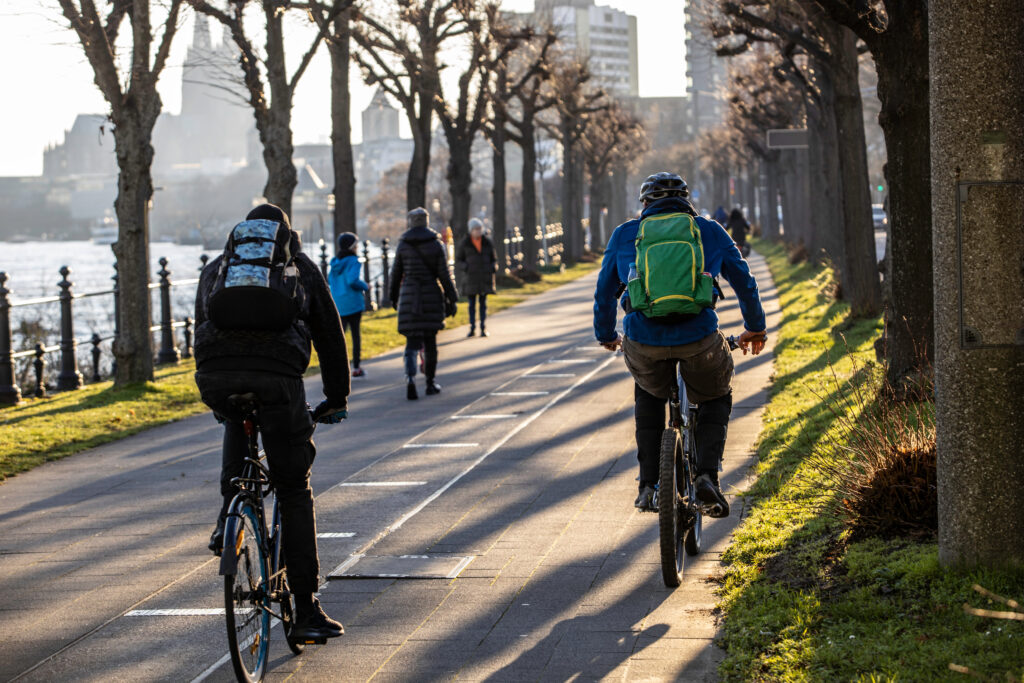 Ein Radweg mit dem Rhein an der linken Seite. Auf dem Weg sind einige Radfahrer zu sehen.